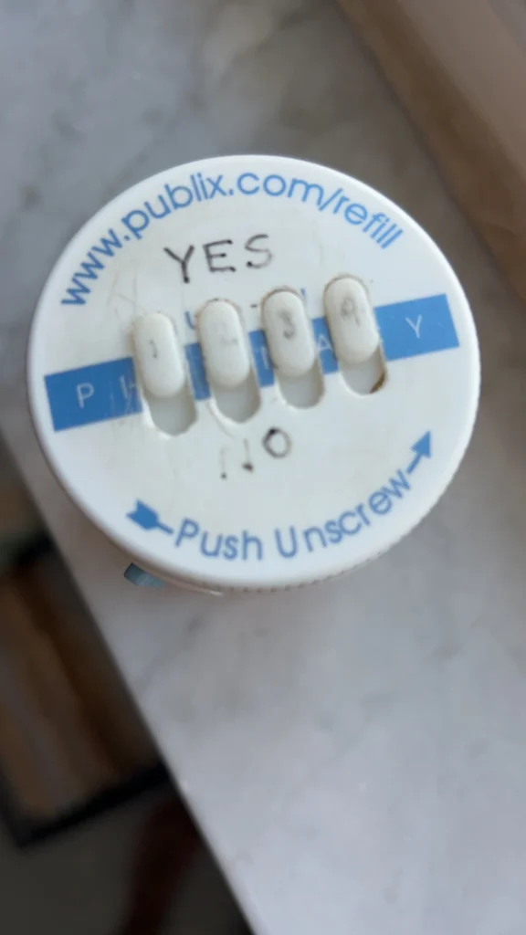 The image shows the top of a white pill bottle cap, likely from a pharmacy